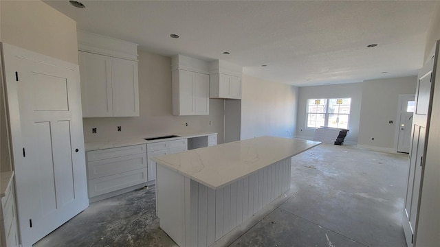 kitchen featuring white cabinetry, light stone counters, concrete flooring, and a center island