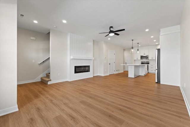 1995 S Warrior Ln, Waukee, IA 50263 - unfurnished living room featuring ceiling fan, recessed lighting, stairs, light wood finished floors, and baseboards