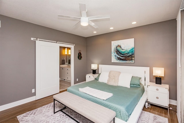 bedroom featuring ensuite bath, wood-type flooring, a barn door, and ceiling fan