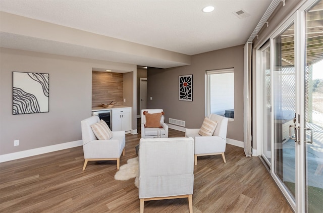 living area featuring beverage cooler, a textured ceiling, and light wood-type flooring