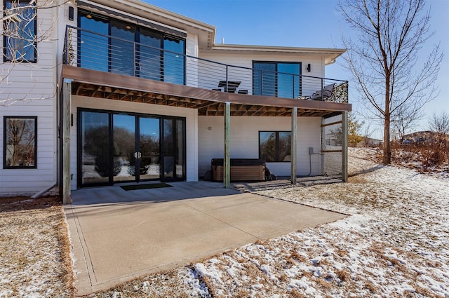 snow covered house featuring a hot tub, a balcony, and a patio area