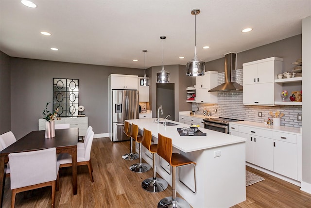 kitchen featuring stainless steel appliances, white cabinetry, a kitchen island with sink, and wall chimney exhaust hood