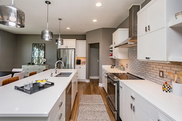 kitchen with stainless steel appliances, wall chimney range hood, a center island with sink, and white cabinets