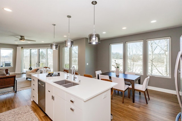 kitchen featuring hanging light fixtures, stainless steel dishwasher, white cabinets, and a center island with sink