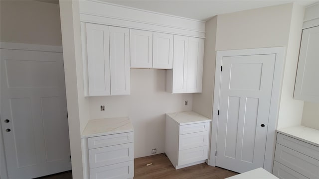 kitchen featuring white cabinets, light stone countertops, and wood finished floors