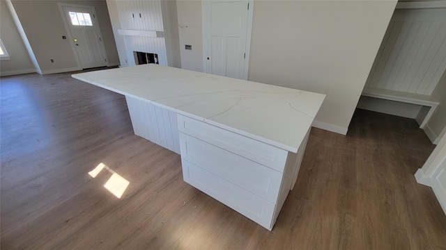 kitchen with a kitchen island, baseboards, light stone countertops, a fireplace, and wood finished floors