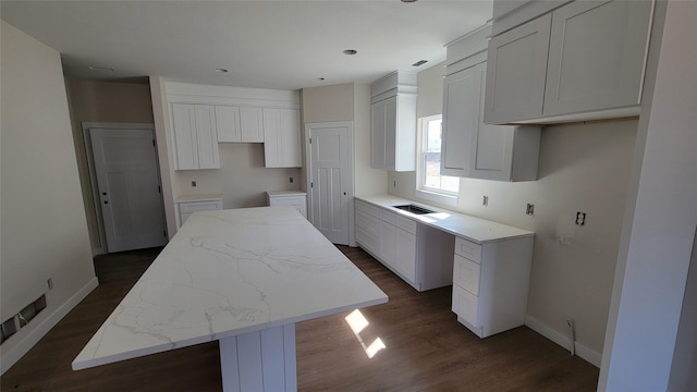 kitchen featuring light stone counters, baseboards, a kitchen island, dark wood finished floors, and white cabinets