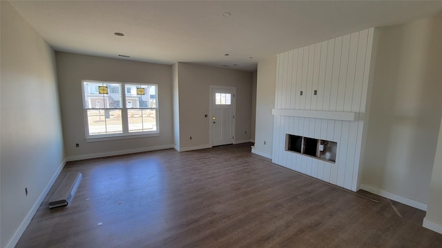 unfurnished living room with baseboards, a large fireplace, and dark wood-type flooring