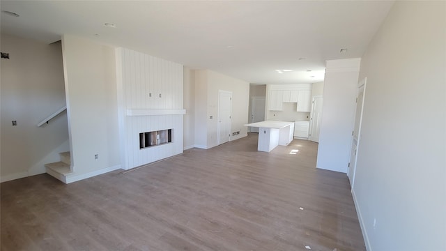 unfurnished living room featuring baseboards, wood finished floors, a fireplace, and stairs