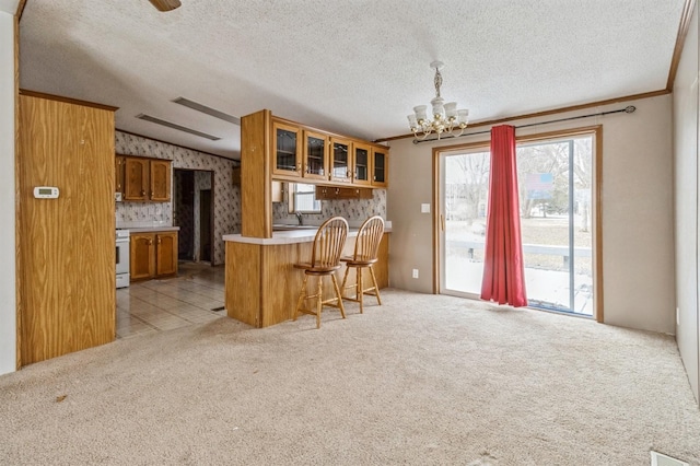 kitchen featuring a kitchen bar, kitchen peninsula, a chandelier, pendant lighting, and light colored carpet