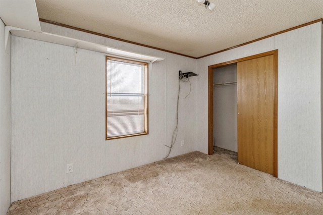 unfurnished bedroom with a textured ceiling, ornamental molding, a closet, and carpet flooring