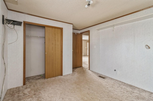 unfurnished bedroom featuring a closet, ornamental molding, a textured ceiling, and light colored carpet