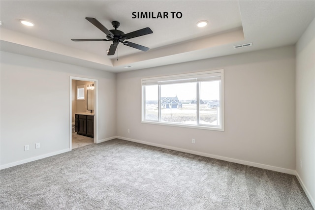 unfurnished bedroom with light carpet, ceiling fan, ensuite bathroom, and a raised ceiling