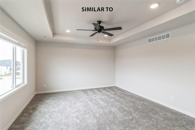 carpeted empty room with ceiling fan, a tray ceiling, and a healthy amount of sunlight