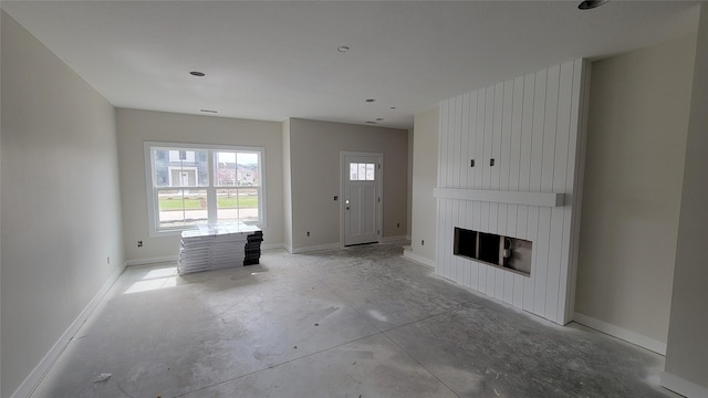 unfurnished living room featuring unfinished concrete floors, baseboards, and a large fireplace