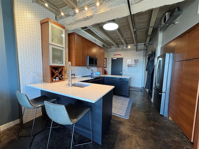 kitchen featuring sink, a kitchen bar, tasteful backsplash, track lighting, and stainless steel refrigerator