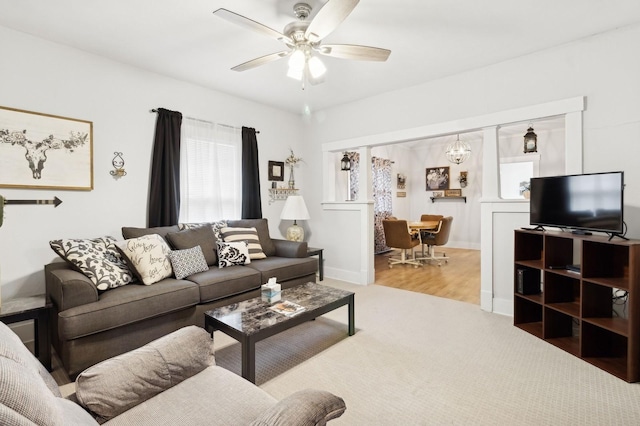 carpeted living room with ceiling fan with notable chandelier