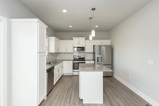 kitchen featuring appliances with stainless steel finishes, pendant lighting, a kitchen island, sink, and white cabinetry