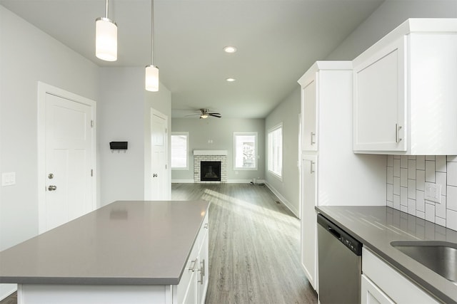 kitchen with dishwasher, pendant lighting, a kitchen island, a brick fireplace, and white cabinets