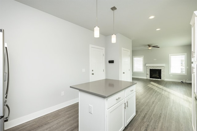 kitchen featuring decorative light fixtures, white cabinets, ceiling fan, a brick fireplace, and a kitchen island