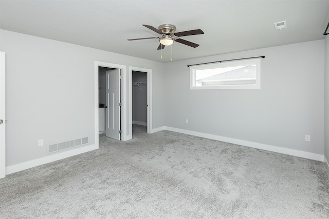 unfurnished bedroom featuring ceiling fan, a walk in closet, a closet, and light carpet