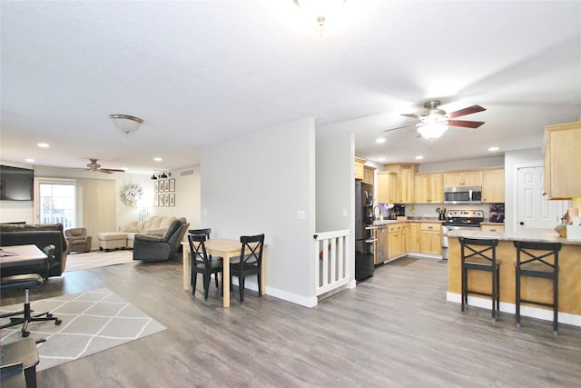 kitchen with stainless steel appliances, kitchen peninsula, a breakfast bar area, wood-type flooring, and light brown cabinetry