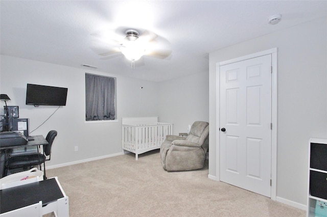 bedroom featuring a nursery area, light carpet, and ceiling fan