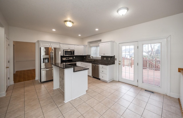 kitchen with a kitchen island, white cabinetry, decorative backsplash, light tile patterned floors, and stainless steel appliances