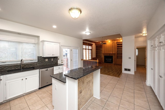 kitchen featuring sink, dishwasher, dark stone countertops, a fireplace, and white cabinets