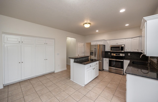 kitchen with appliances with stainless steel finishes, white cabinetry, sink, dark stone countertops, and light tile patterned floors