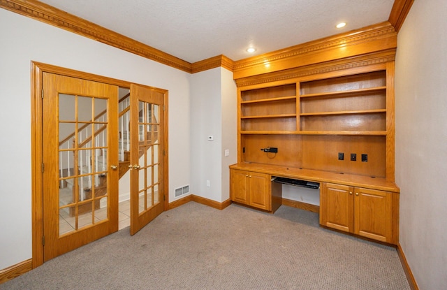 home office with built in desk, ornamental molding, light colored carpet, a textured ceiling, and french doors