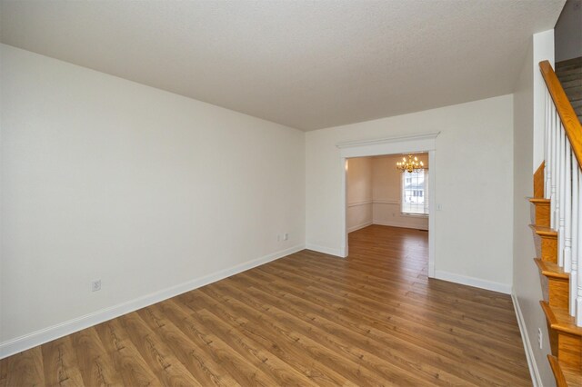 empty room featuring a notable chandelier, hardwood / wood-style flooring, and a textured ceiling