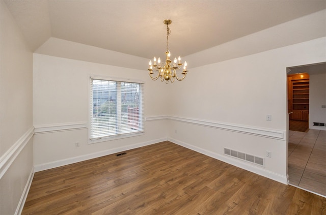 spare room featuring hardwood / wood-style flooring, vaulted ceiling, a notable chandelier, and a tray ceiling