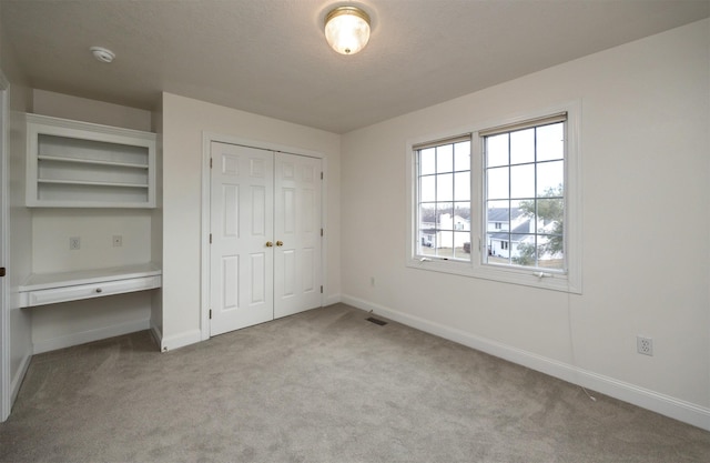 unfurnished bedroom featuring a closet, built in desk, and light carpet