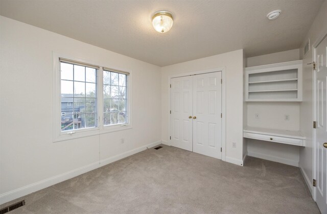 unfurnished bedroom featuring built in desk, light colored carpet, a closet, and a textured ceiling