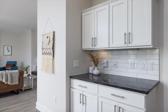 bar featuring white cabinetry, dark stone countertops, tasteful backsplash, and light hardwood / wood-style flooring