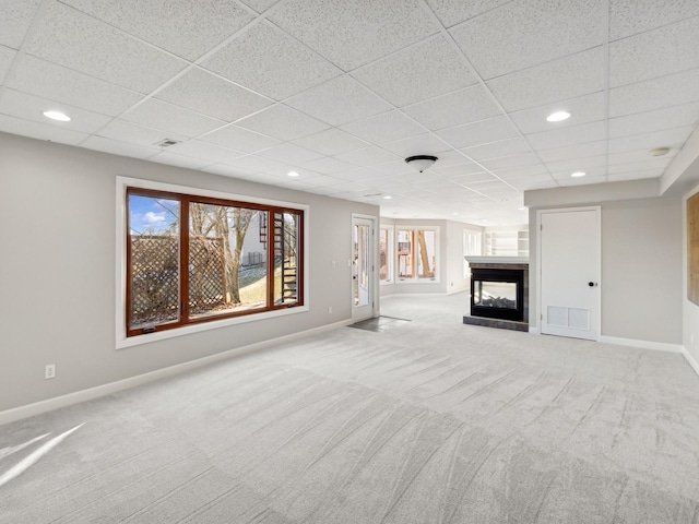 unfurnished living room with a paneled ceiling, a multi sided fireplace, and light carpet