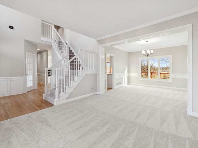 unfurnished living room featuring light colored carpet, crown molding, and an inviting chandelier