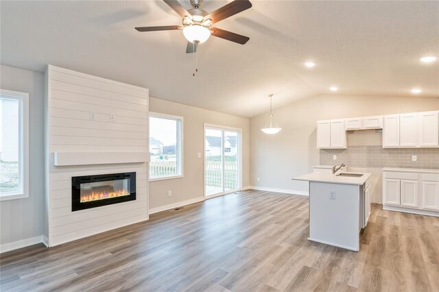 kitchen with decorative light fixtures, a fireplace, white cabinetry, tasteful backsplash, and a center island with sink