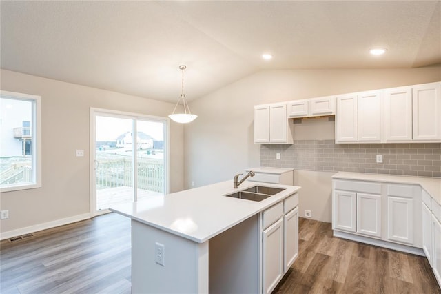 kitchen with visible vents, an island with sink, vaulted ceiling, light countertops, and white cabinetry