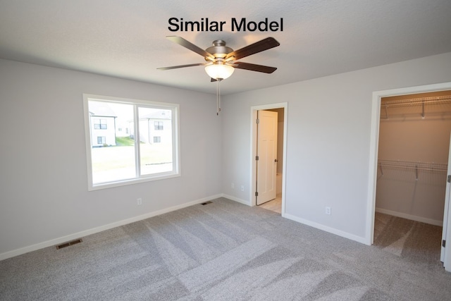 unfurnished bedroom with ceiling fan, light carpet, a closet, and a walk in closet