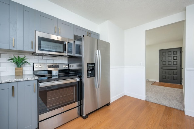 kitchen with light stone countertops, a textured ceiling, light hardwood / wood-style flooring, backsplash, and appliances with stainless steel finishes