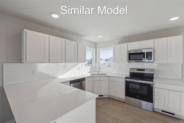 kitchen featuring white cabinetry, appliances with stainless steel finishes, decorative backsplash, light hardwood / wood-style flooring, and sink