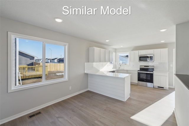 kitchen with kitchen peninsula, appliances with stainless steel finishes, decorative backsplash, and white cabinetry