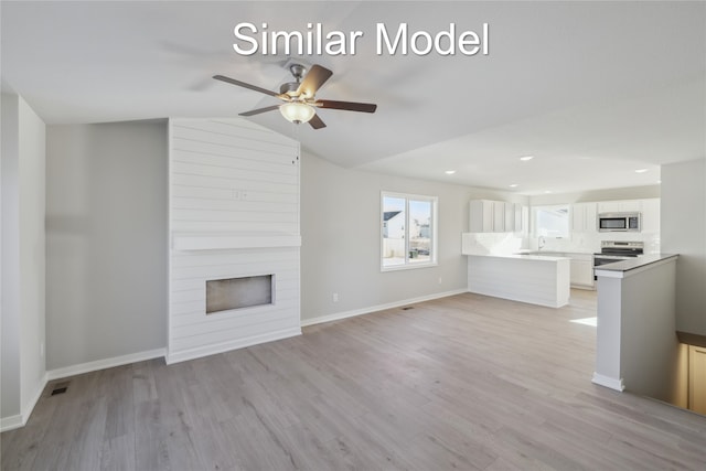 unfurnished living room with ceiling fan, vaulted ceiling, a fireplace, sink, and light hardwood / wood-style flooring