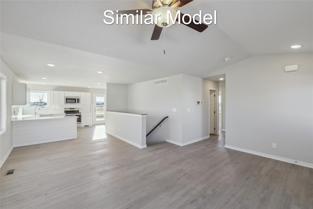 unfurnished living room with ceiling fan, vaulted ceiling, sink, and light hardwood / wood-style floors