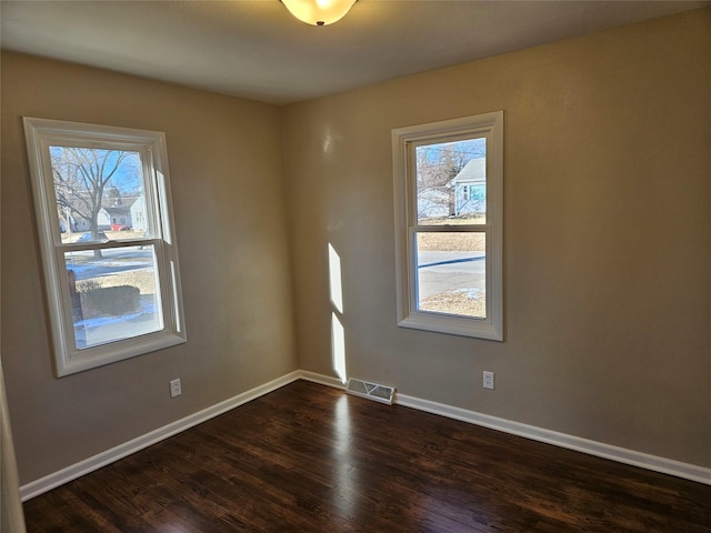 spare room featuring a healthy amount of sunlight and dark hardwood / wood-style flooring