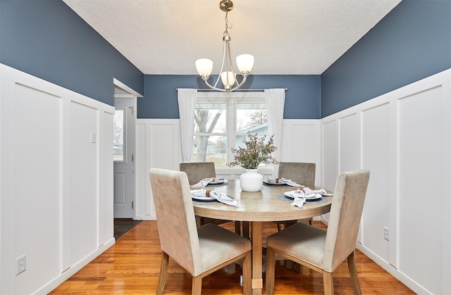 dining space with a textured ceiling, a chandelier, and light hardwood / wood-style floors