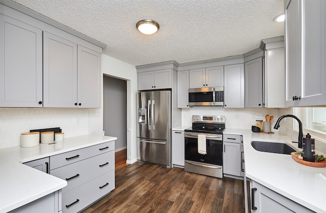 kitchen featuring gray cabinetry, stainless steel appliances, dark wood-type flooring, sink, and tasteful backsplash