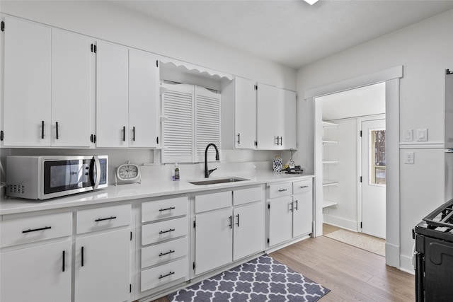 kitchen featuring black range with gas cooktop, white cabinetry, light hardwood / wood-style flooring, and sink